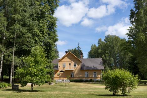 Kollane armas maja roheluses suurte puude vahel