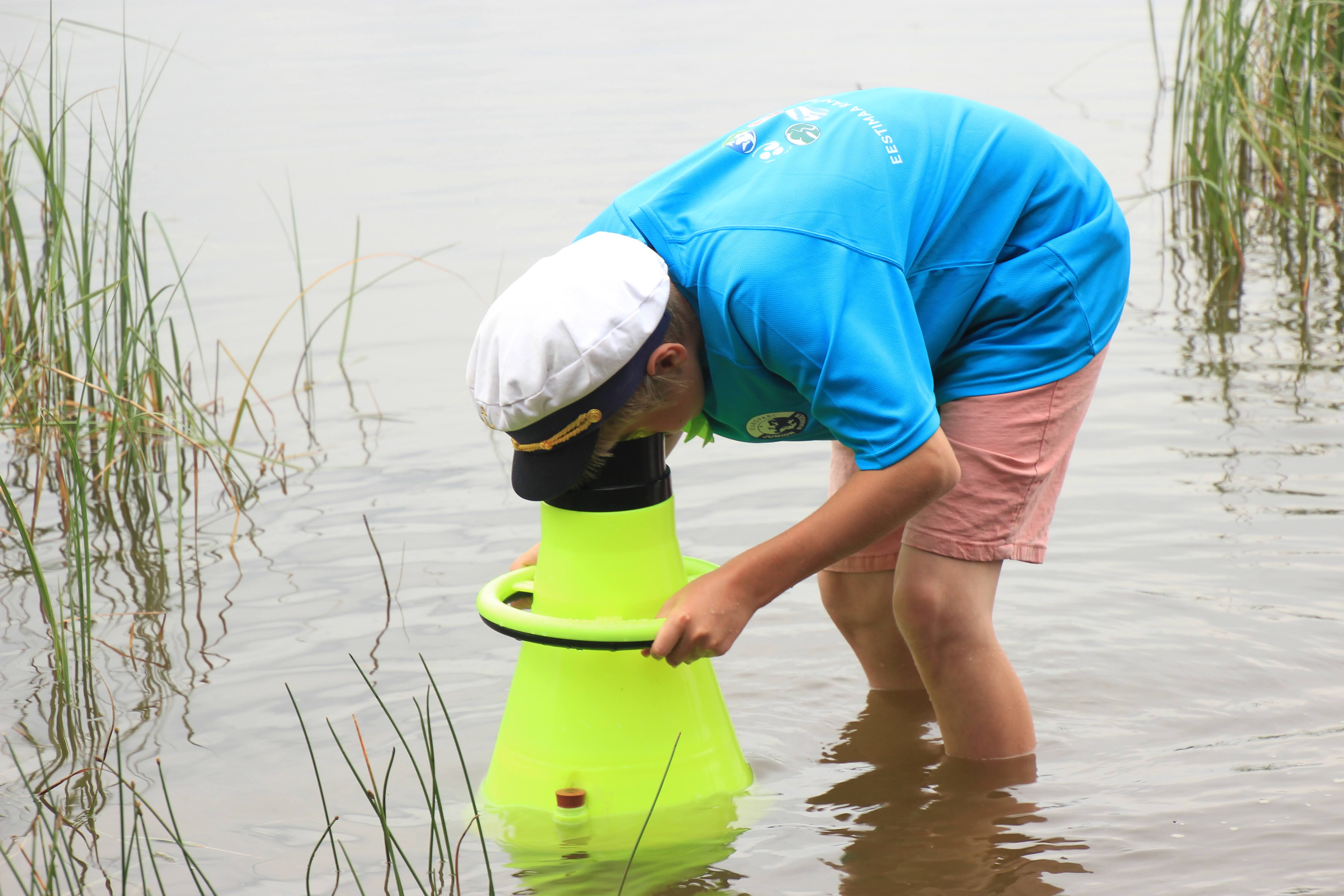 Sisise särgi ja meremehemütsiga noormees seisab järves ja uurib vee-elustikku
