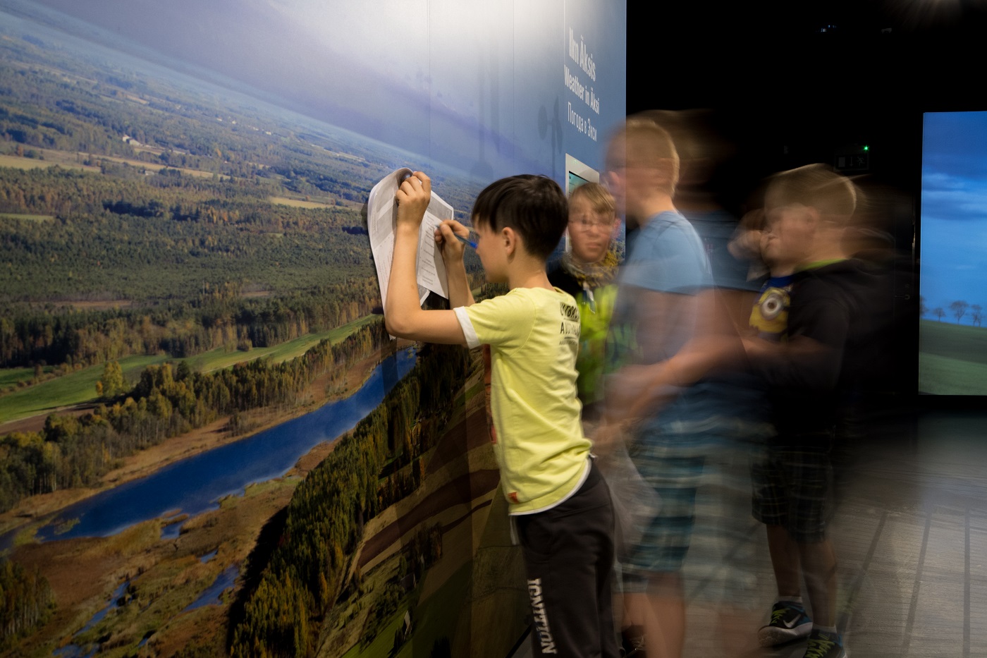 lapsed lahendavad ülesandeid looduspildiga stendi ees