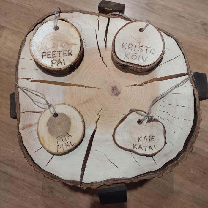 Lõhki kuivanud puupakul on neli oksast ristlõikena lõigatud puust medalit, medalitele on põletatud perekonnanimed Kõiv, Katai, Pihl, Pai